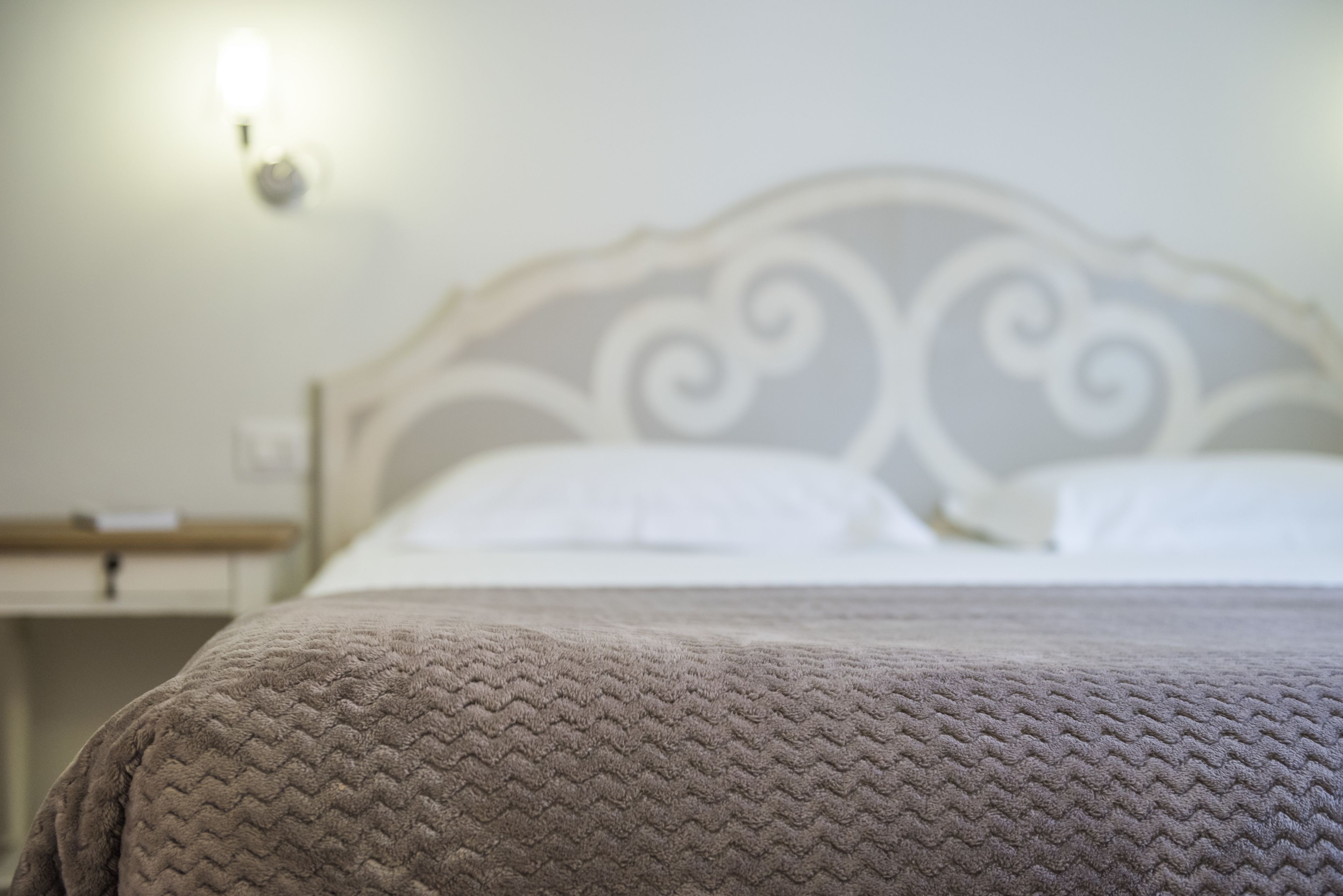 Uma cama com manta texturizada e cabeceira branca com design decorativo.