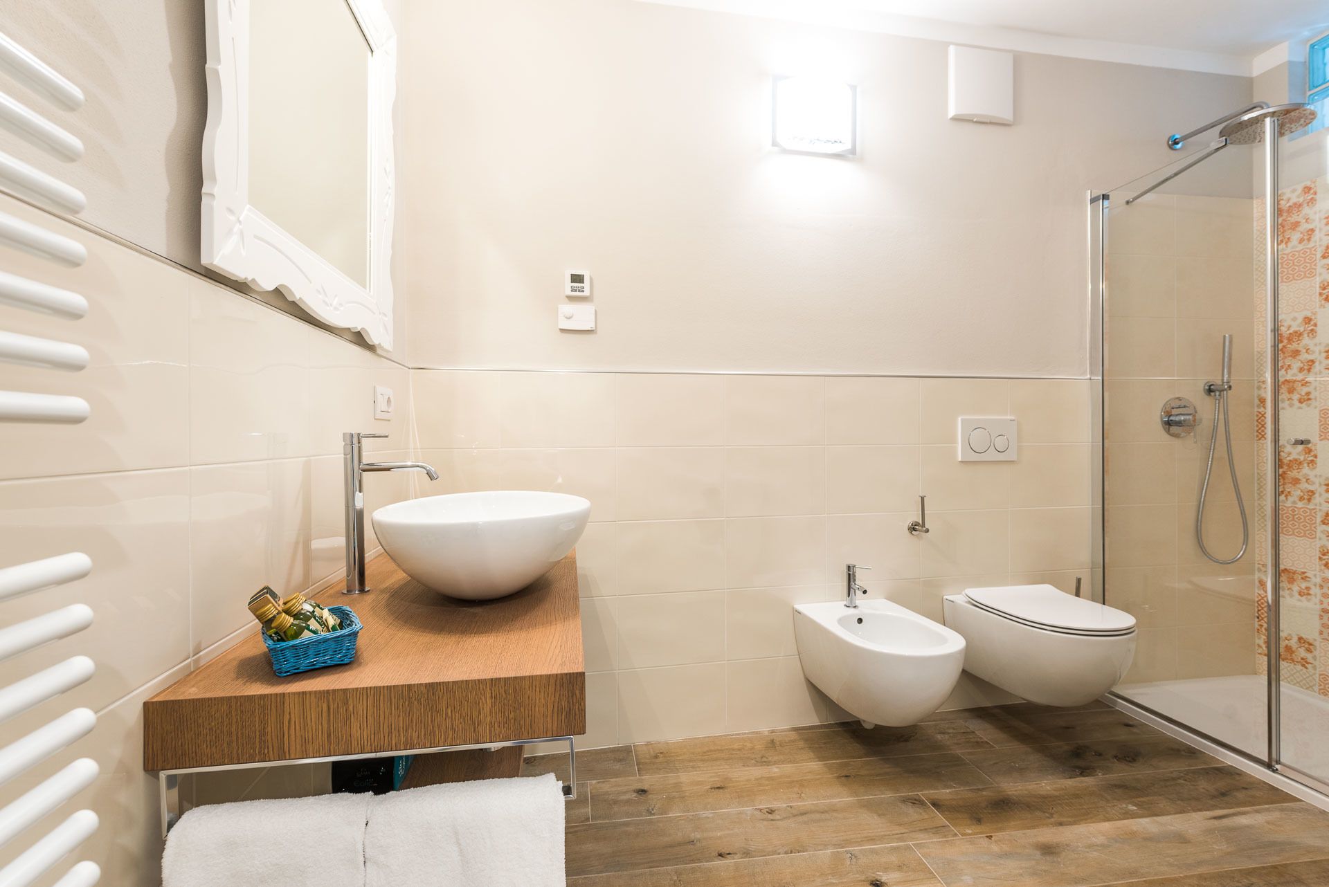 Een moderne badkamer met een wastafel op voet, een bidet, een toilet en een douche met glazen wand.