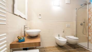 Een moderne badkamer met een wastafel op voet, een bidet, een toilet en een douche met glazen wand.