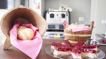 Una cesta de madera con un pan, un paño rosa y un cubo de madera con pan, además de un plato de vidrio con porciones de tarta de frutos rojos.
