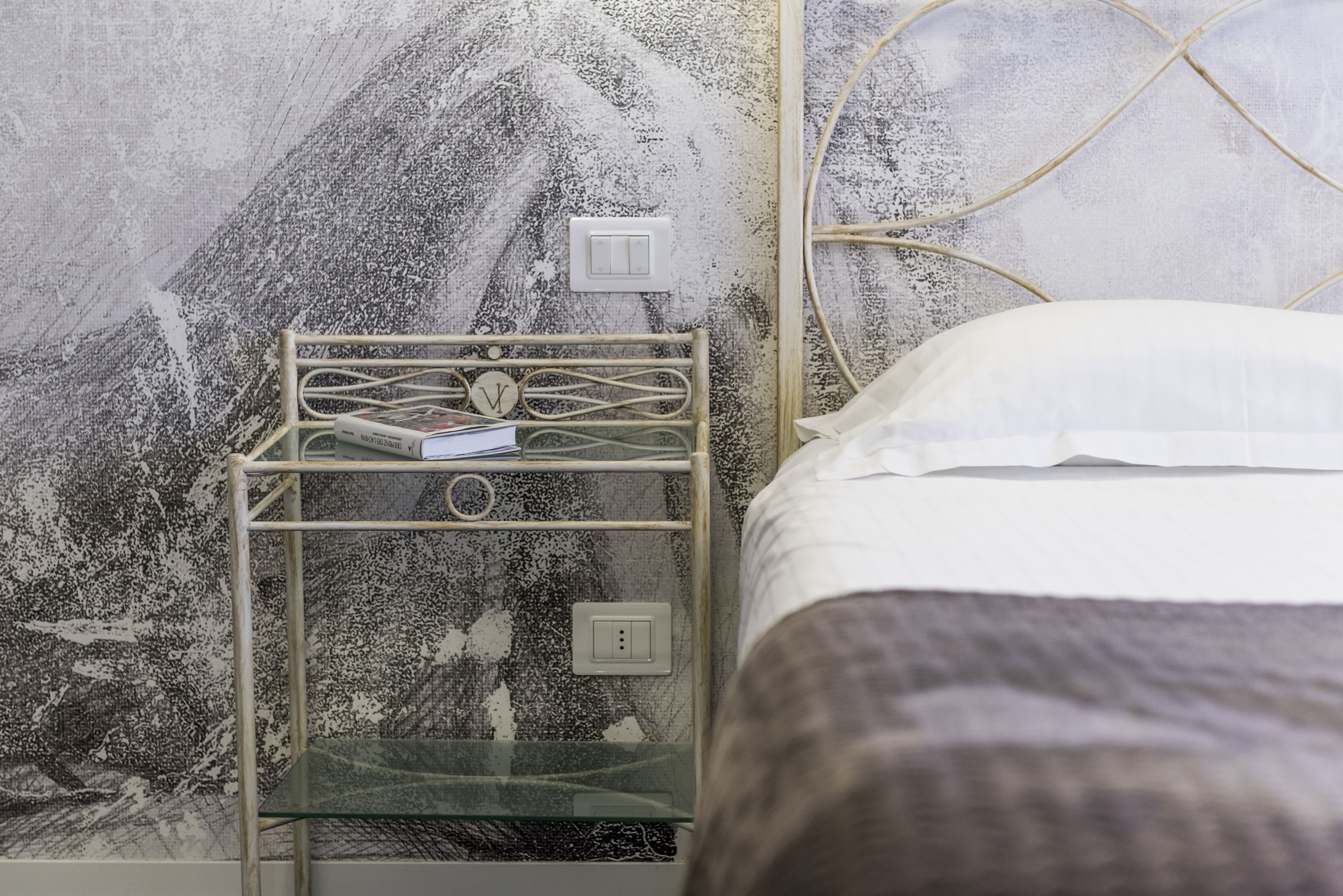 A bed with a white pillow and a metal nightstand with a glass shelf.