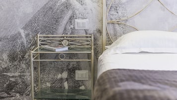A bed with a white pillow and a metal nightstand with a glass shelf.