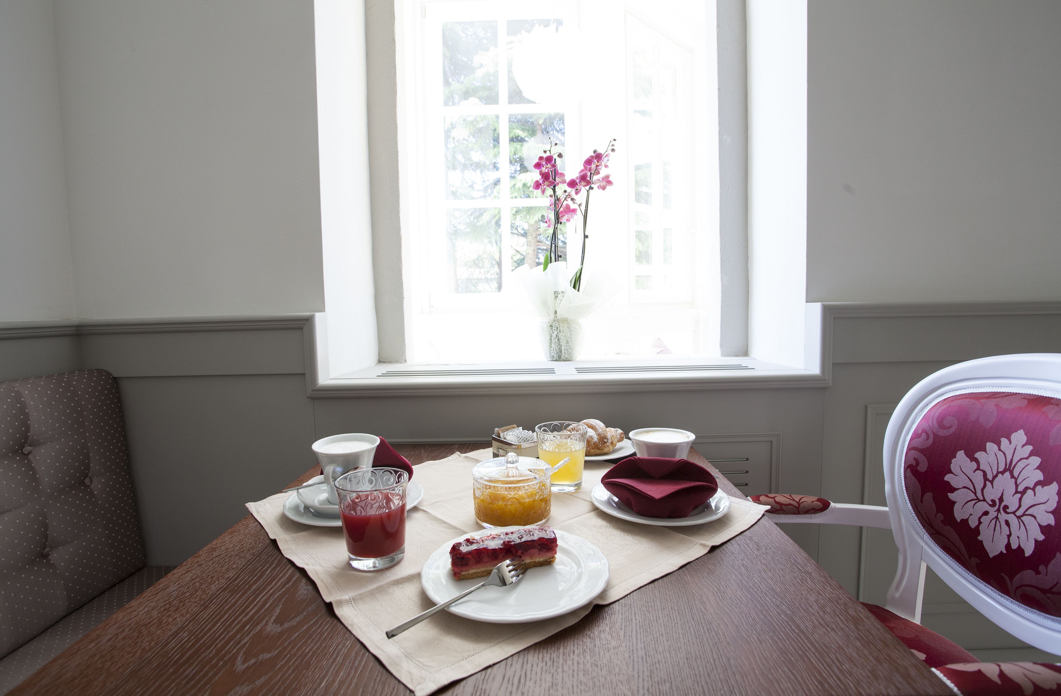 Una mesa de comedor con una comida preparada junto a una ventana, que incluye un plato de comida, un vaso de jugo y una taza.