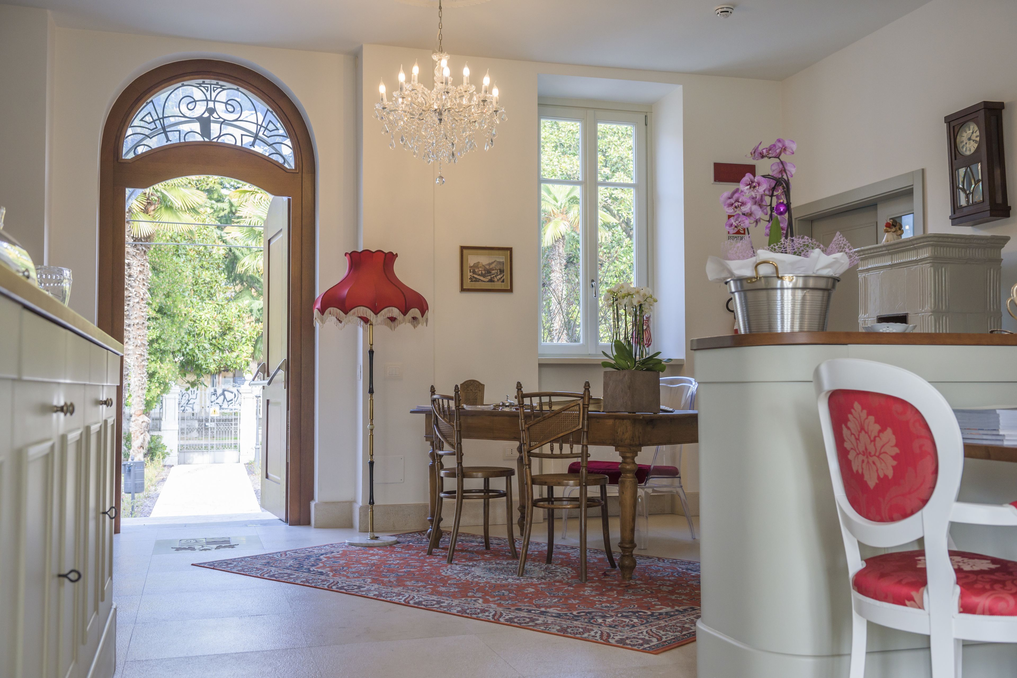 A dining area with a chandelier, a red lamp, and a view of the outdoors through a large window.