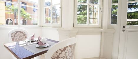 A corner room with a dining table set for two, large windows, and white walls.