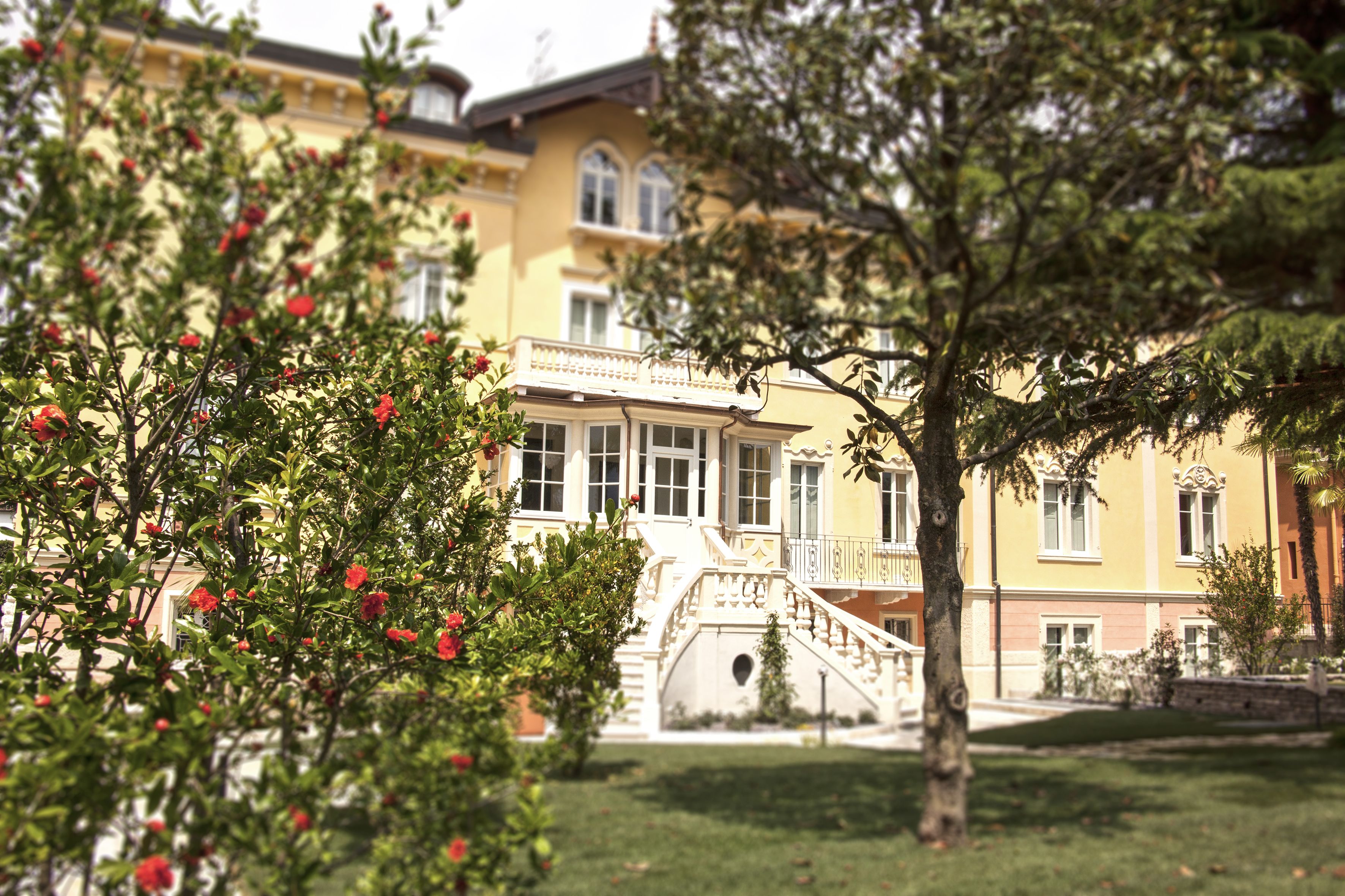 A building with a staircase leading to a balcony, surrounded by greenery and trees.