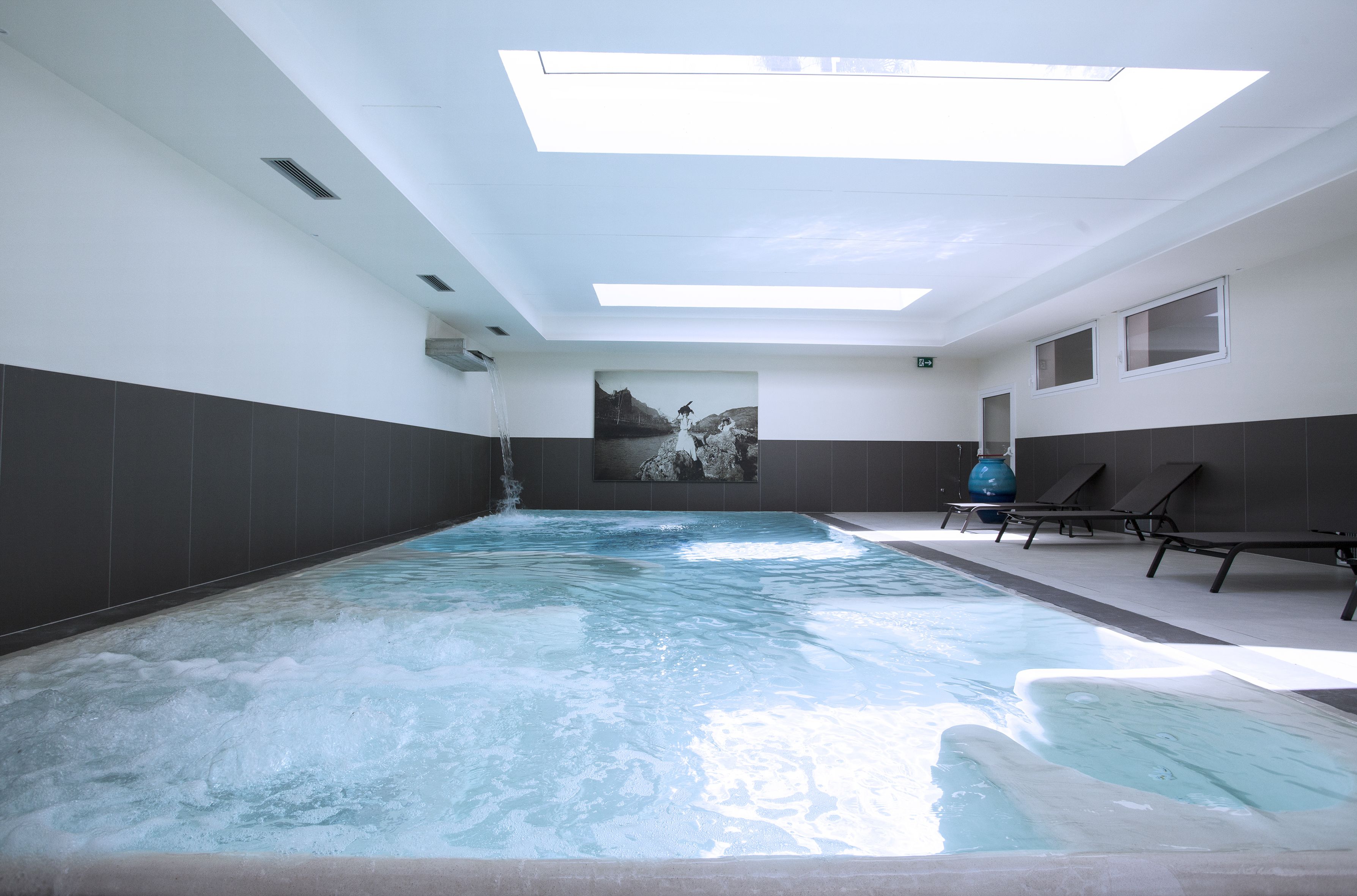 A swimming pool with a skylight, lounge chairs, and a large wall mural.