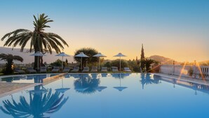 A clear swimming pool with lounge chairs and umbrellas, surrounded by palm trees and a mountain backdrop. - Paradise Hotel Corfu (Corfu)