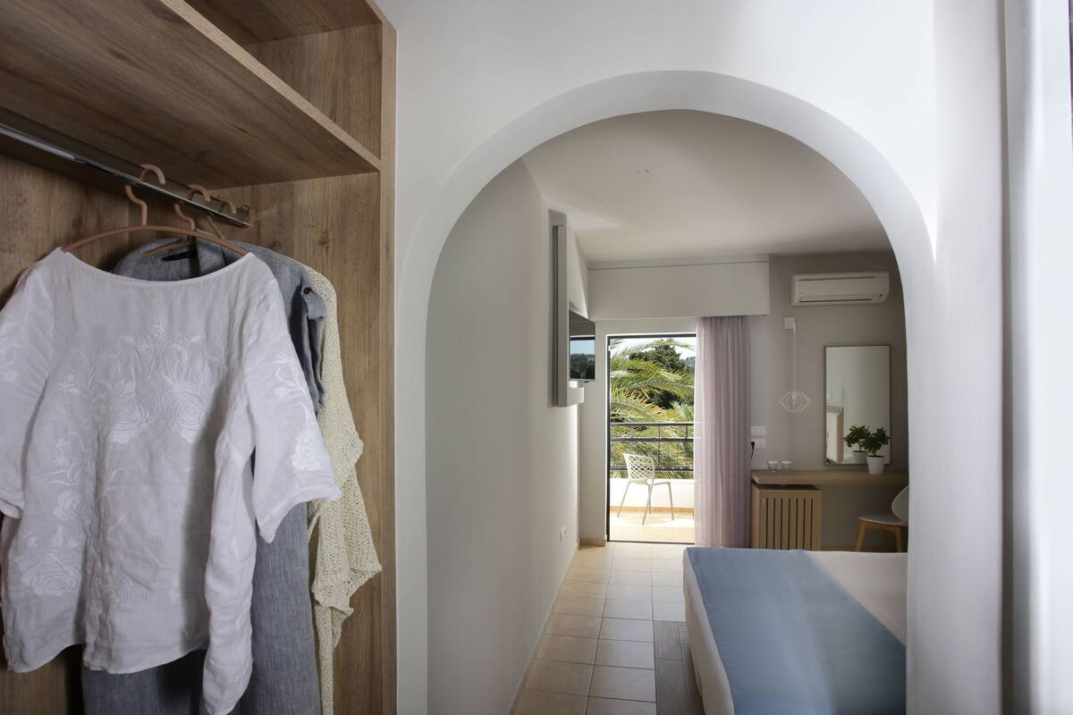 A hallway leading to a balcony with a view of palm trees, a wooden wardrobe, and a bench.