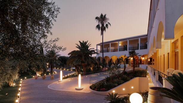 A hotel courtyard with a paved walkway, palm trees, and a large planter. - Paradise Hotel Corfu (Corfu)