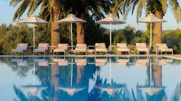 Una piscina con agua cristalina azul, rodeada de sillones de playa y sombrillas, con palmeras al fondo.