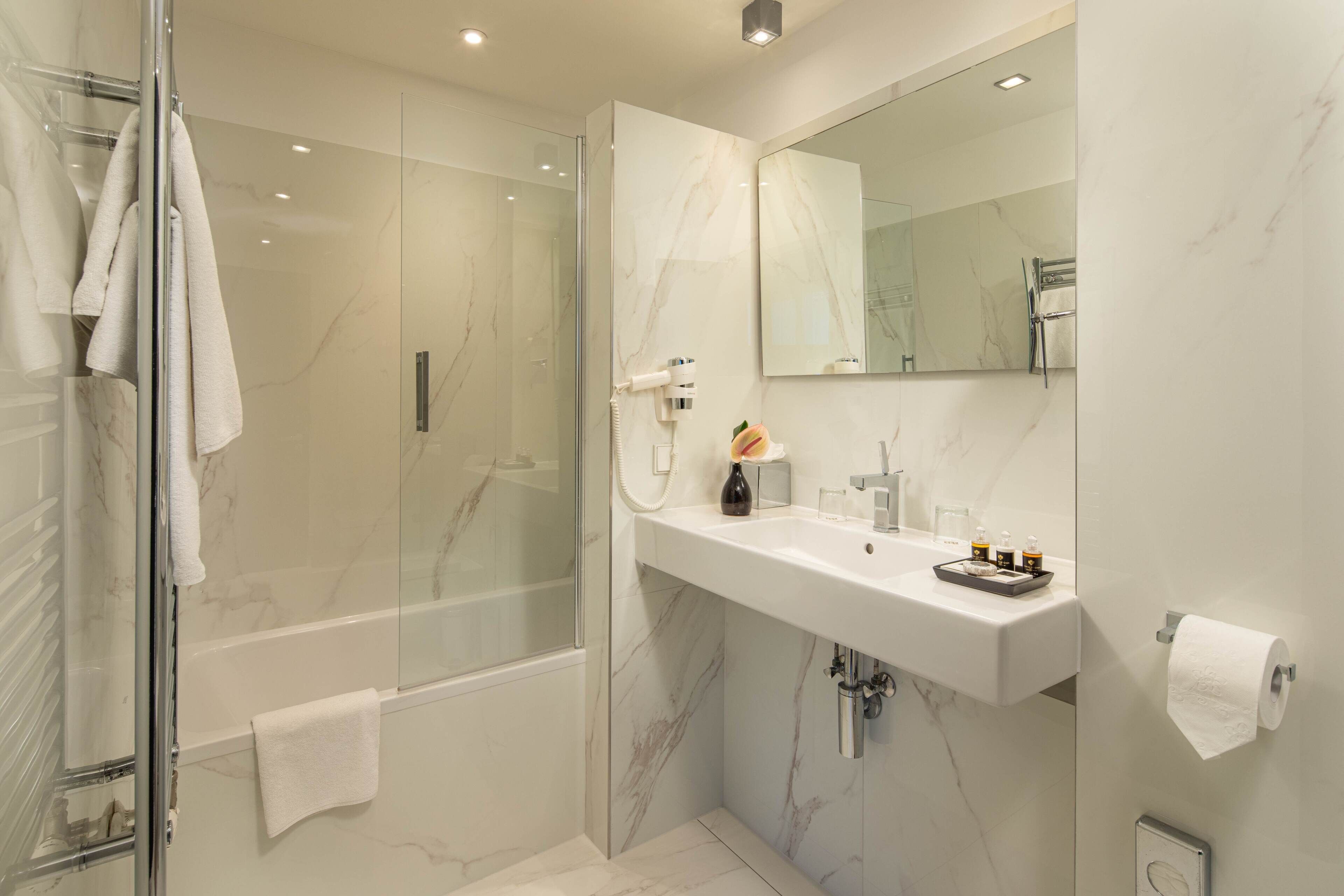 A modern bathroom with a glass-enclosed shower, a marble sink, and a large mirror.