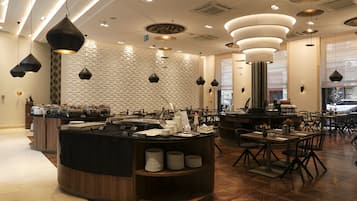 A modern restaurant interior with a central counter, multiple dining tables, and hanging pendant lights.