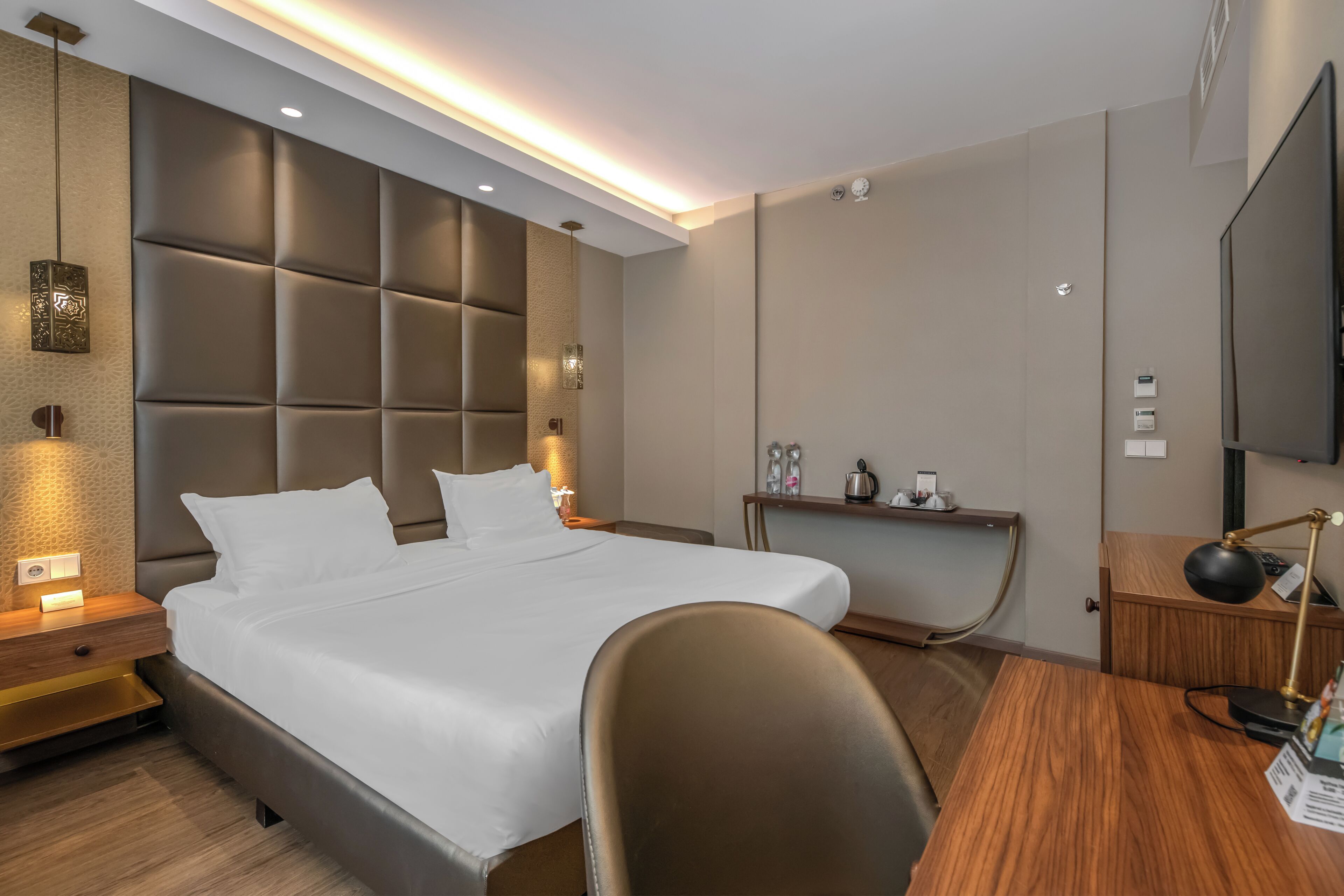 Una habitación de hotel moderna con una cama grande, un escritorio, una silla, un televisor y una mesita de noche con lámpara.