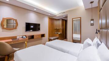 Quarto de hotel com duas camas, uma escrivaninha com cadeira, televisão, espelho e guarda-roupa.