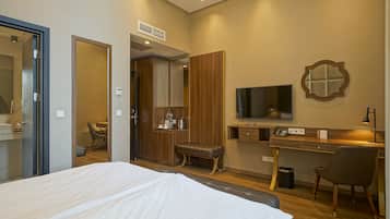 A hotel room with a bed, a desk with a computer, a TV, a mirror, and a small seating area.