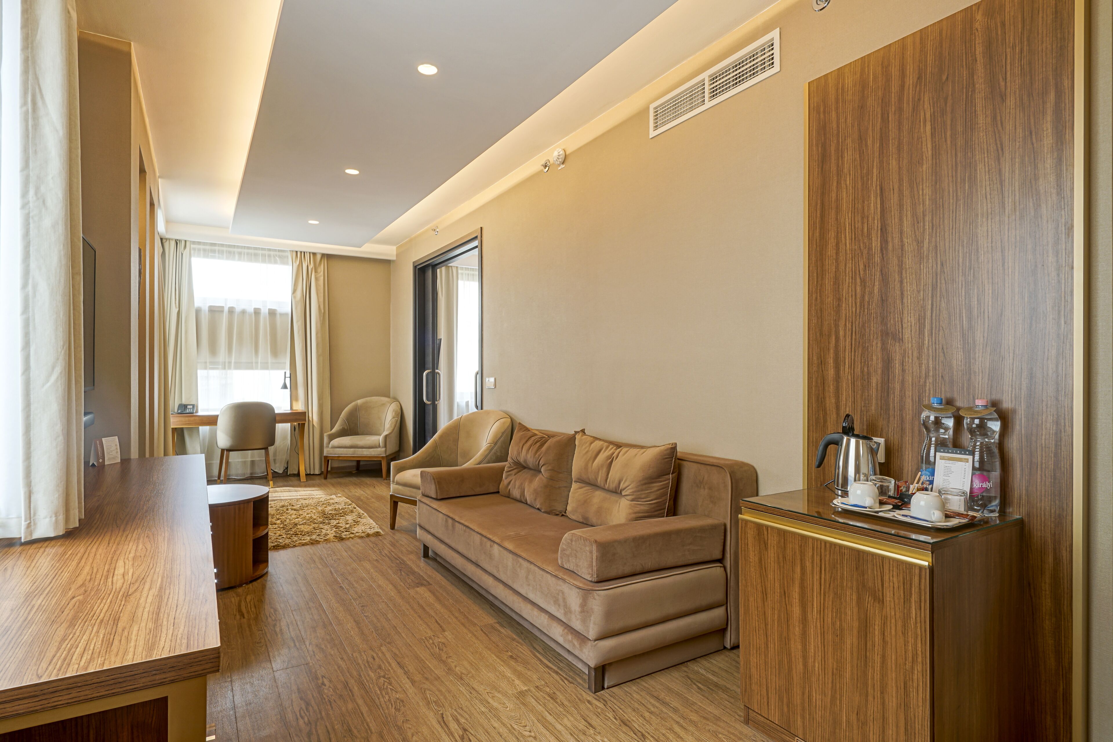 Una habitación de hotel moderna con suelo de madera, un sofá, un escritorio y un minibar.