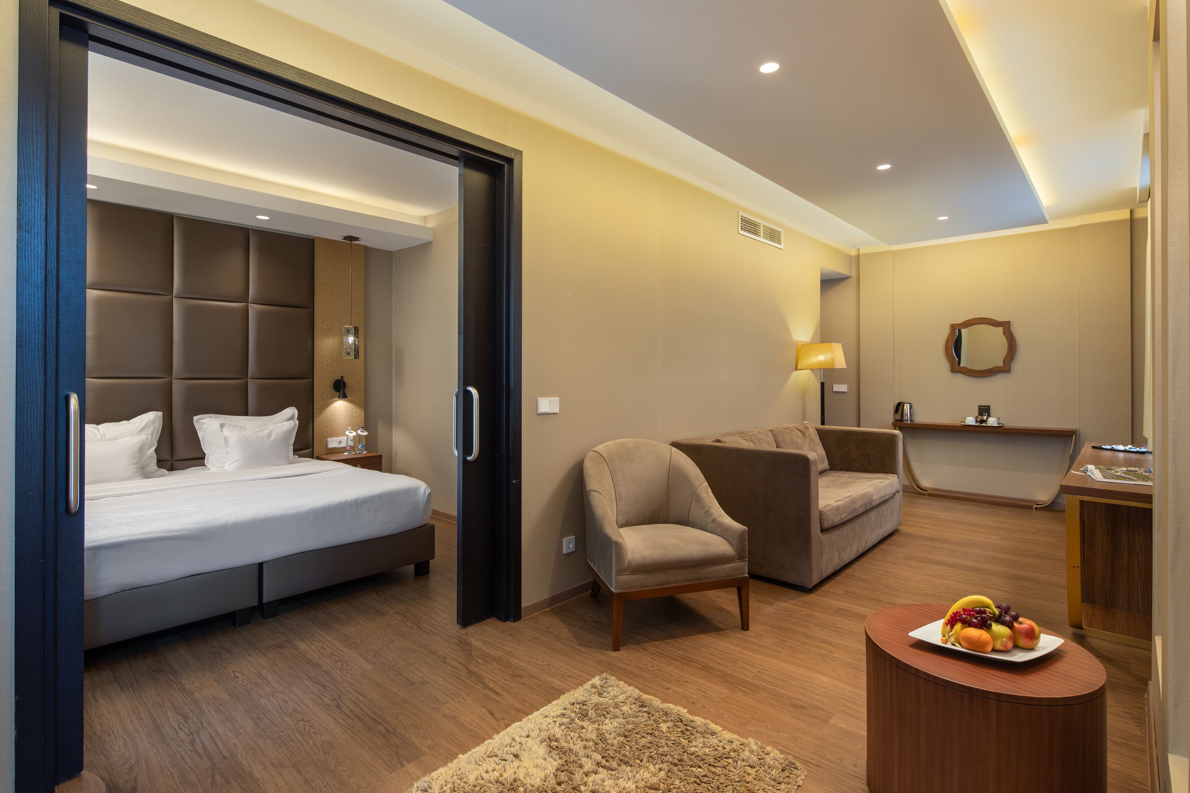 Una habitación de hotel moderna con una cama, un sofá, una mesita con fruta y un escritorio con una lámpara.