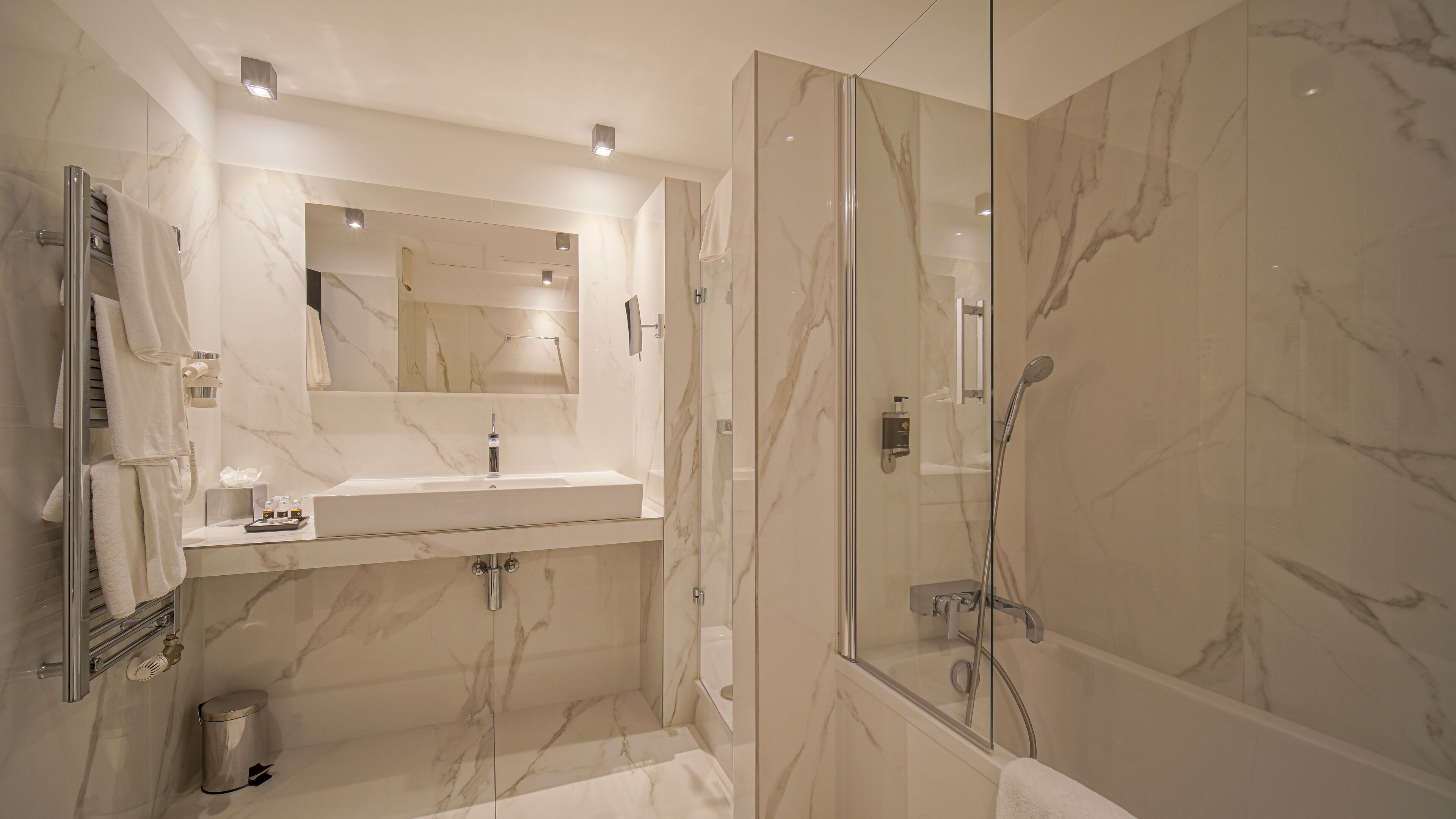 Un baño moderno con ducha de vidrio, tocador con azulejos de mármol y un espejo grande.