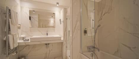 Un baño moderno con ducha de vidrio, tocador con azulejos de mármol y un espejo grande.