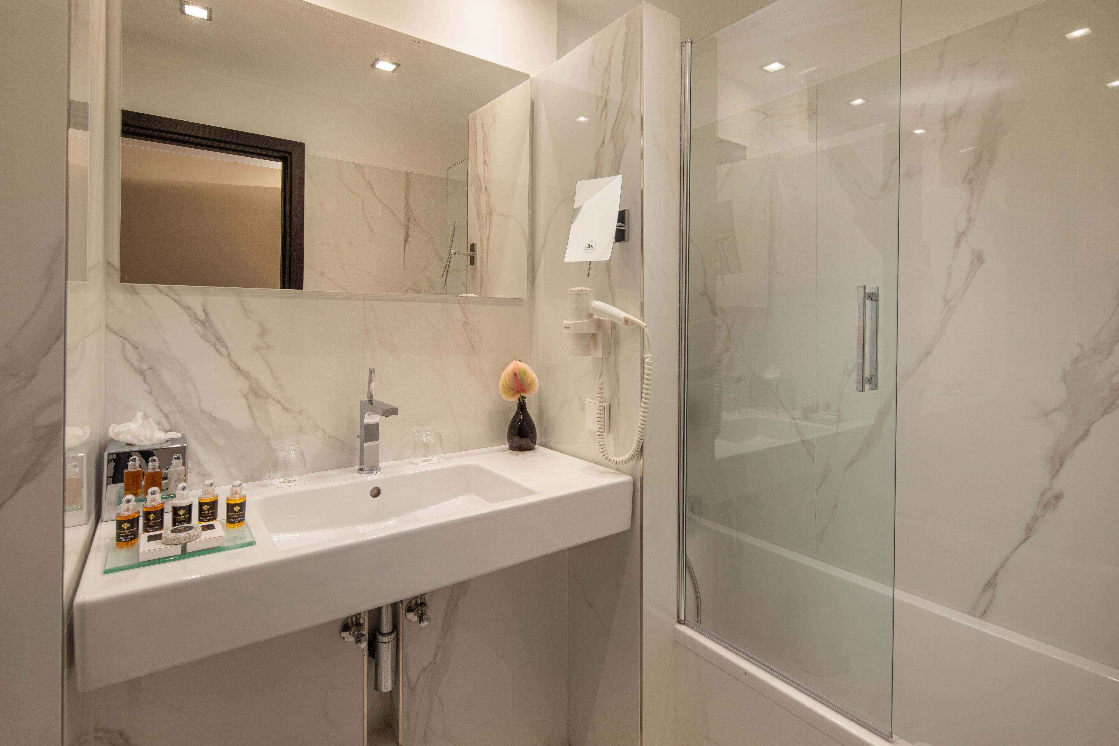 A modern bathroom with a marble sink, a glass shower enclosure, and a large mirror.