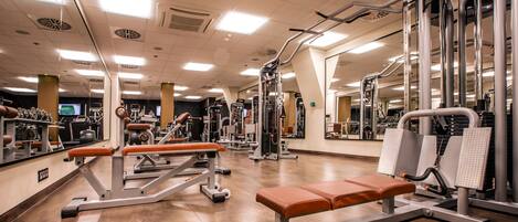 A gym with various exercise machines, a bench, and mirrors on the walls.