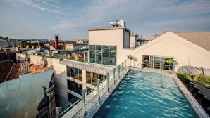 A rooftop pool with glass railings, a modern building with large windows, and a cityscape in the background.