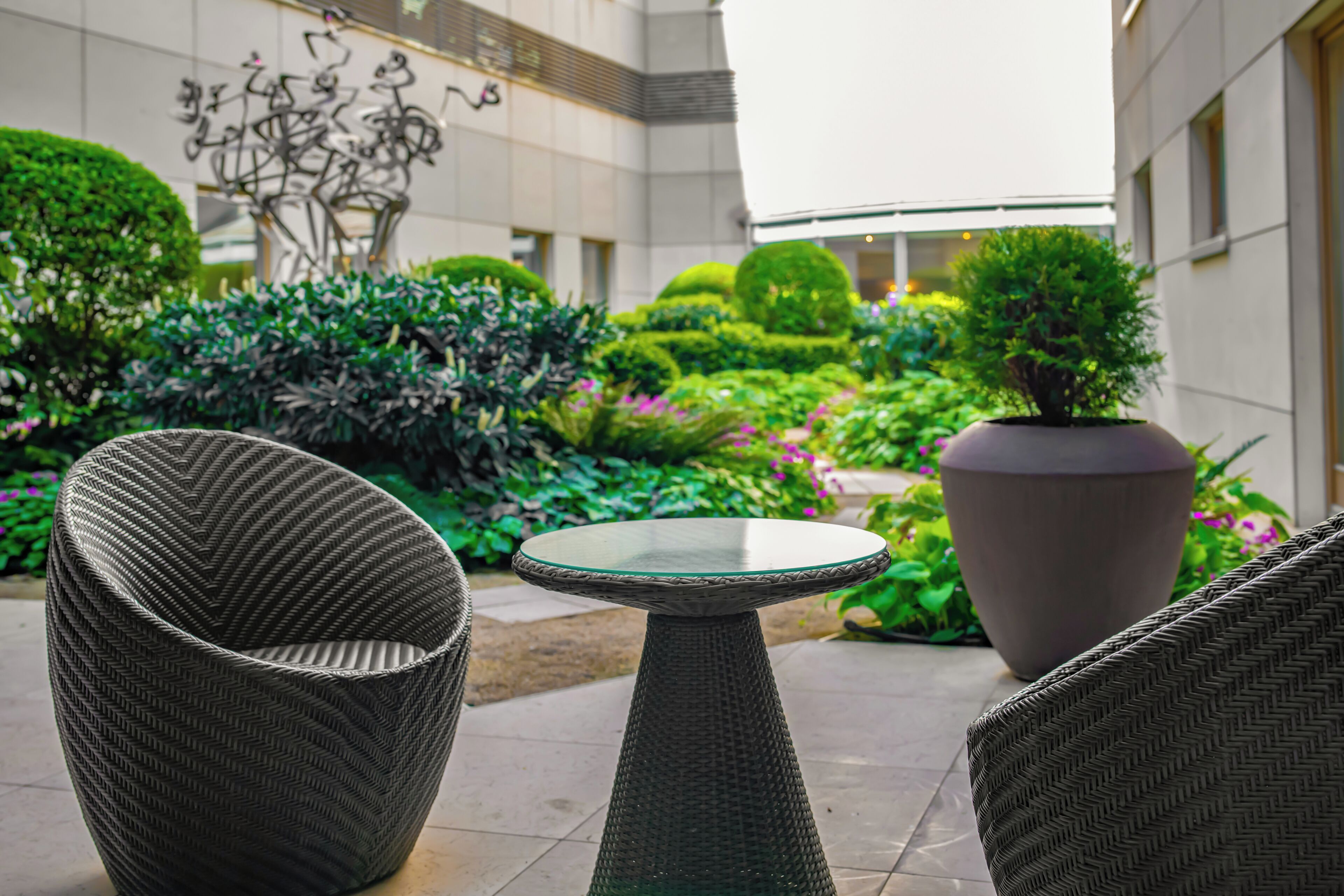 A courtyard with wicker furniture, a glass-top table, and a large planter.