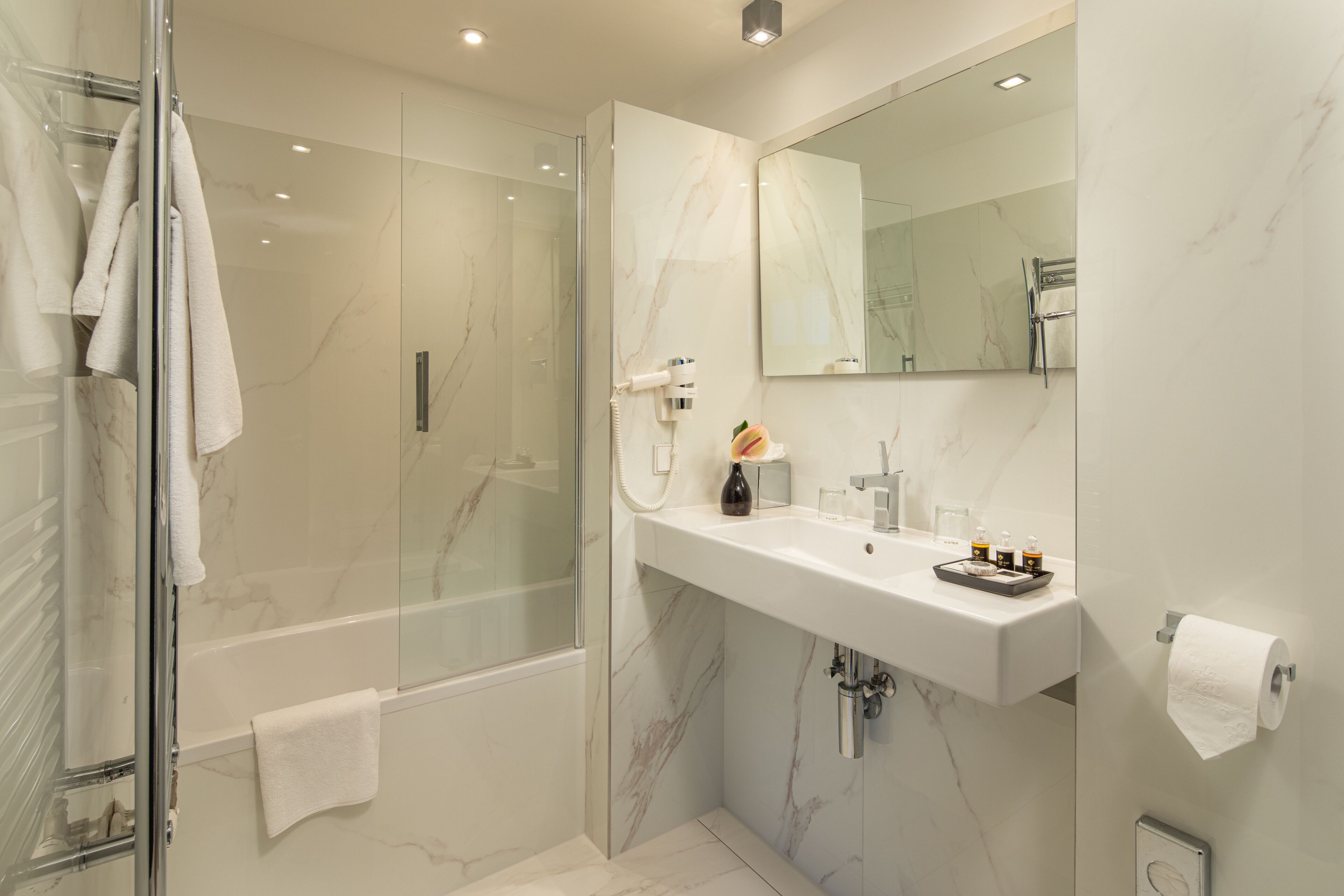 Un baño moderno con ducha de mampara de vidrio, un lavamanos blanco y un espejo grande.