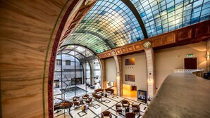 A spacious lobby with a high arched glass ceiling, marble walls, and a central seating area with multiple chairs and tables. - Continental Hotel Budapest (Budapest)