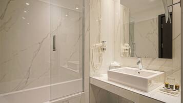 Un baño moderno con cabina de ducha de vidrio, un lavamanos grande con espejo y pared de mármol.
