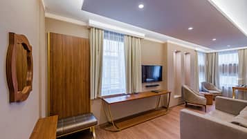 A modern hotel room with a wooden bench, a sofa, a TV, and a desk.