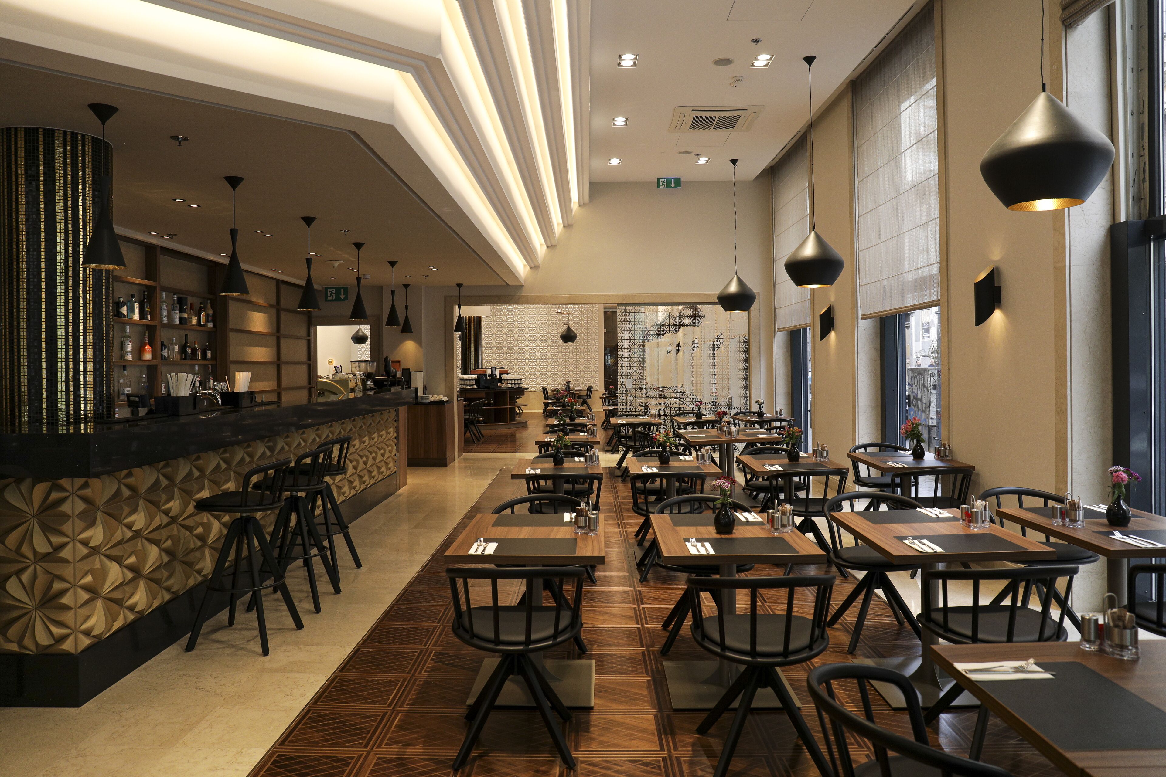 A spacious restaurant with high ceilings, modern pendant lighting, and a variety of seating options including bar stools and tables.