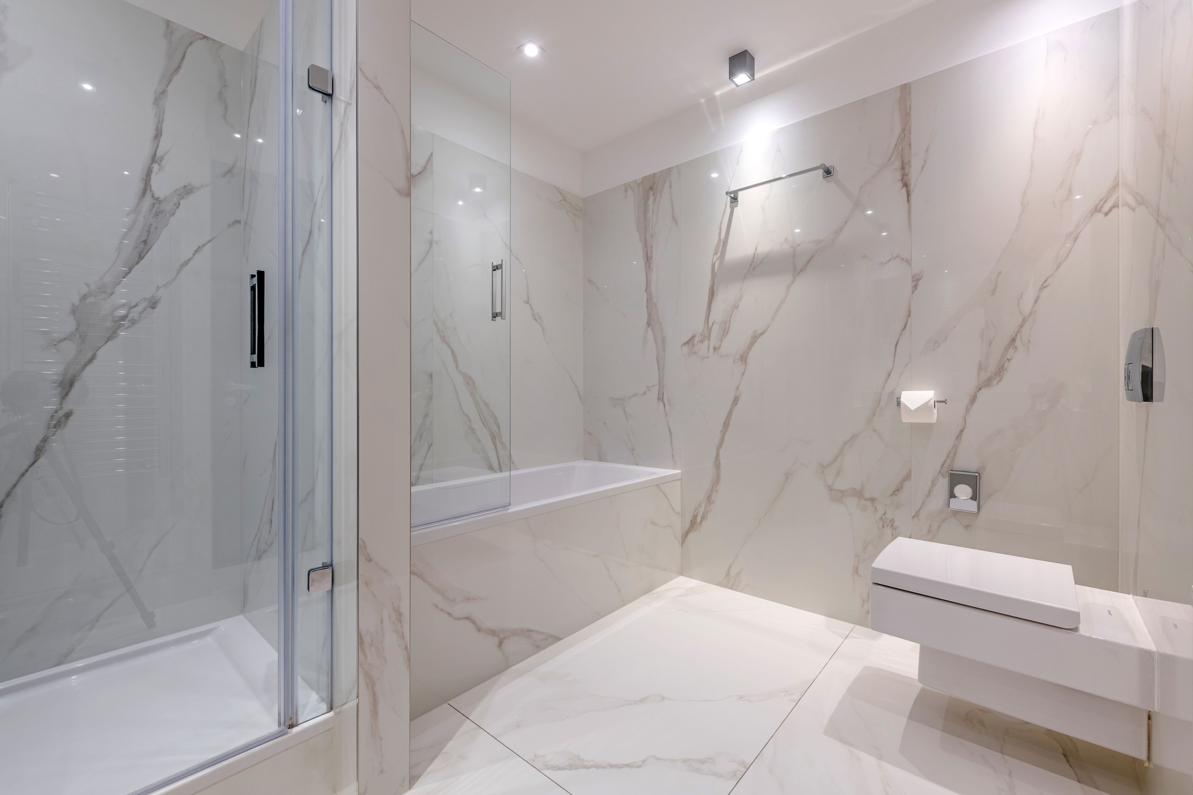 Un bagno moderno con box doccia in vetro, pareti in marmo e mobile lavabo bianco.