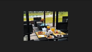 Un espacio de comedor al aire libre con una mesa dispuesta para el desayuno, que incluye bollería, café y zumo de naranja.