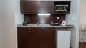 Una cocina compacta con armarios de madera oscura, microondas integrado, refrigerador pequeño y encimera de granito.