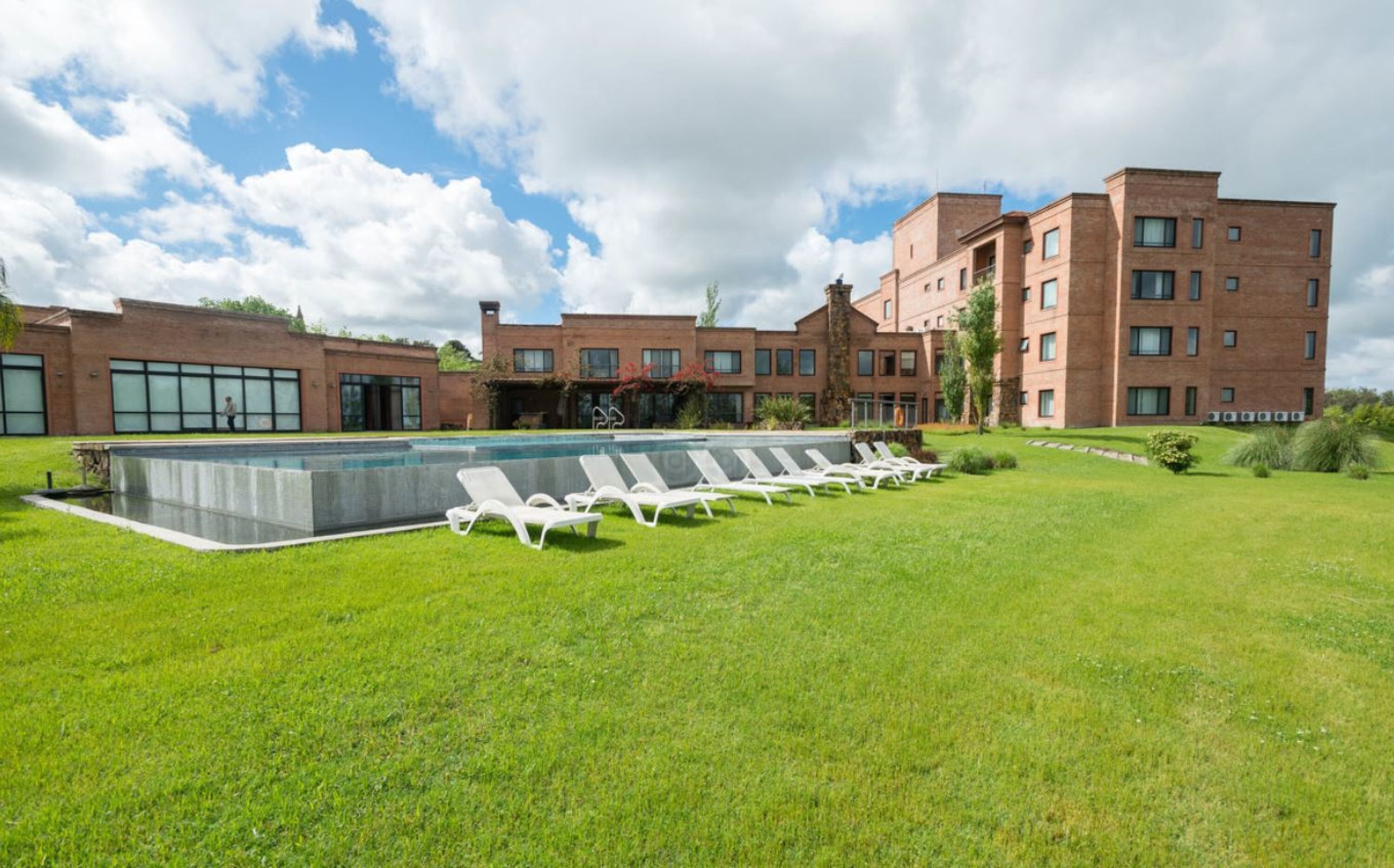 A modern hotel with a swimming pool, lounge chairs, and a well-maintained lawn.