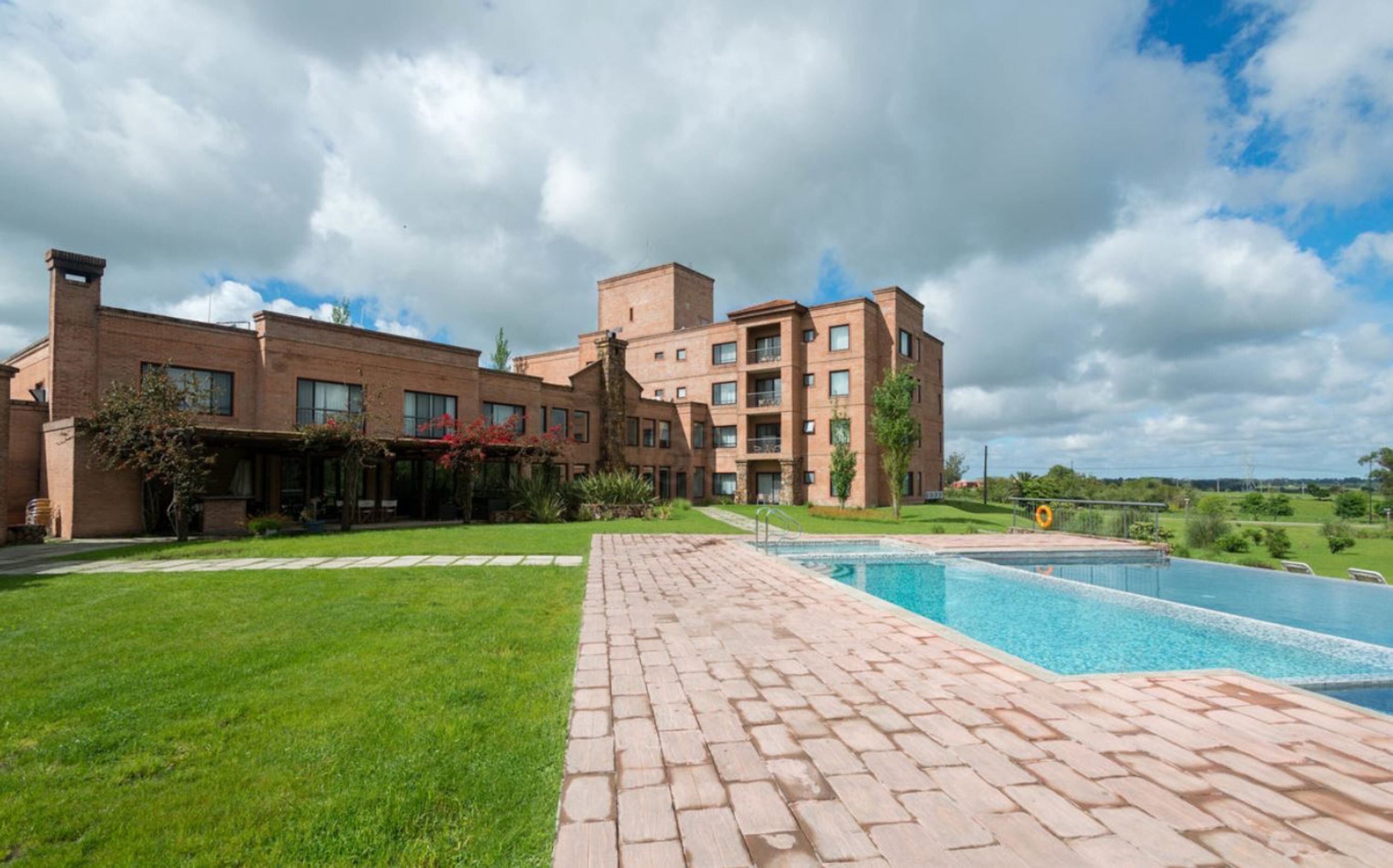 A hotel with a swimming pool, a brick exterior, and a well-maintained lawn.