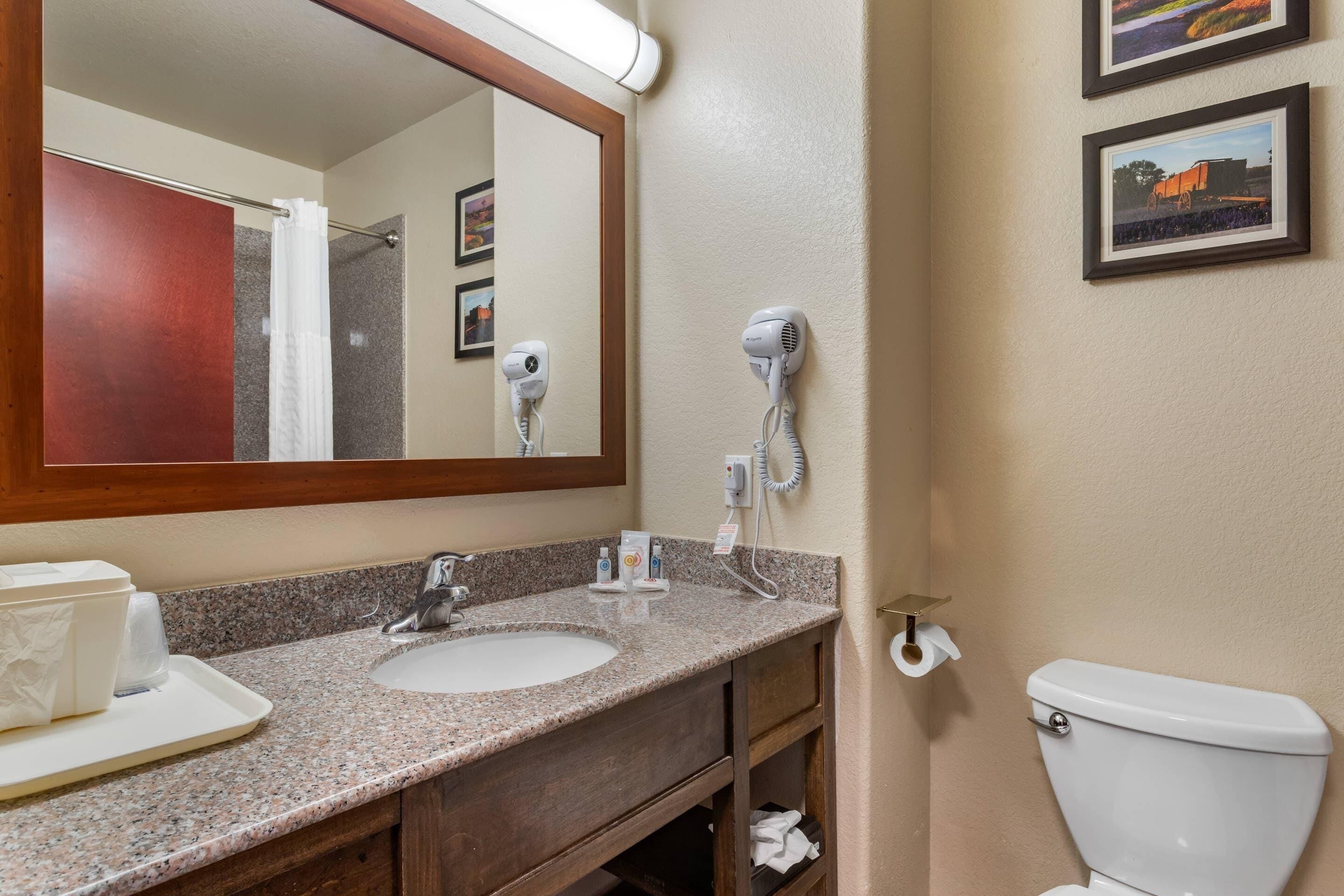 A bathroom with a granite countertop, a sink, a mirror, a hairdryer, and a toilet.