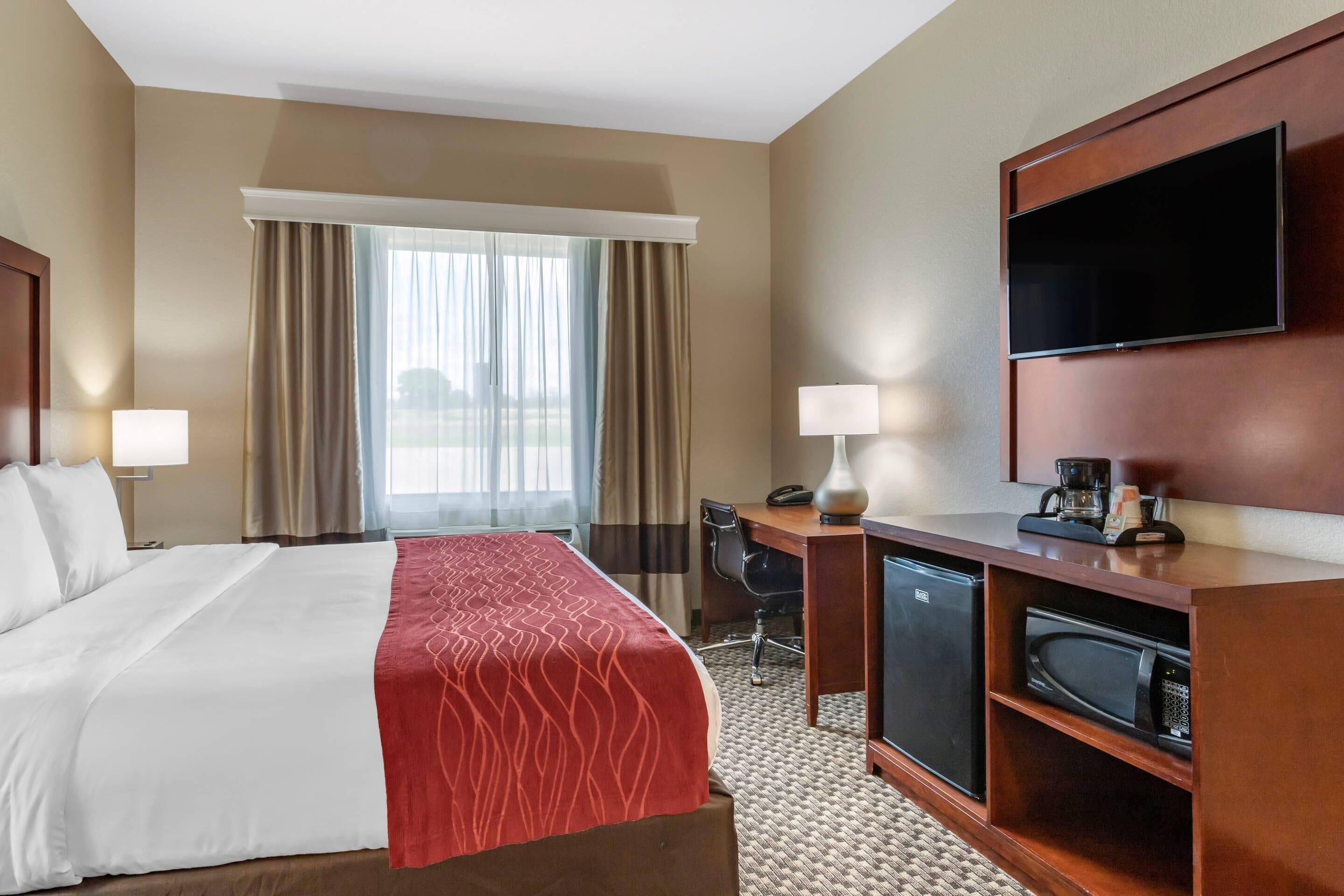 A hotel room with a bed, desk, chair, television, and a refrigerator.