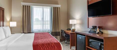 A hotel room with a bed, desk, chair, television, and a refrigerator.