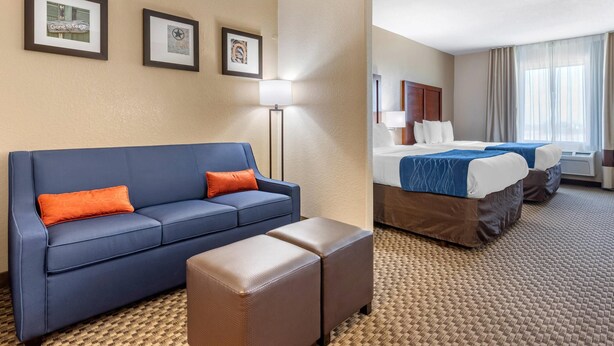 A hotel room with a blue sofa, an ottoman, a bed with a blue bedspread, and two framed pictures on the wall. - Comfort Inn & Suites Navasota (Navasota)