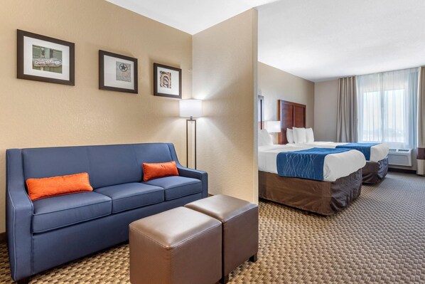 A hotel room with a blue sofa, an ottoman, a bed with a blue bedspread, and two framed pictures on the wall. - Comfort Inn & Suites Navasota (Navasota)