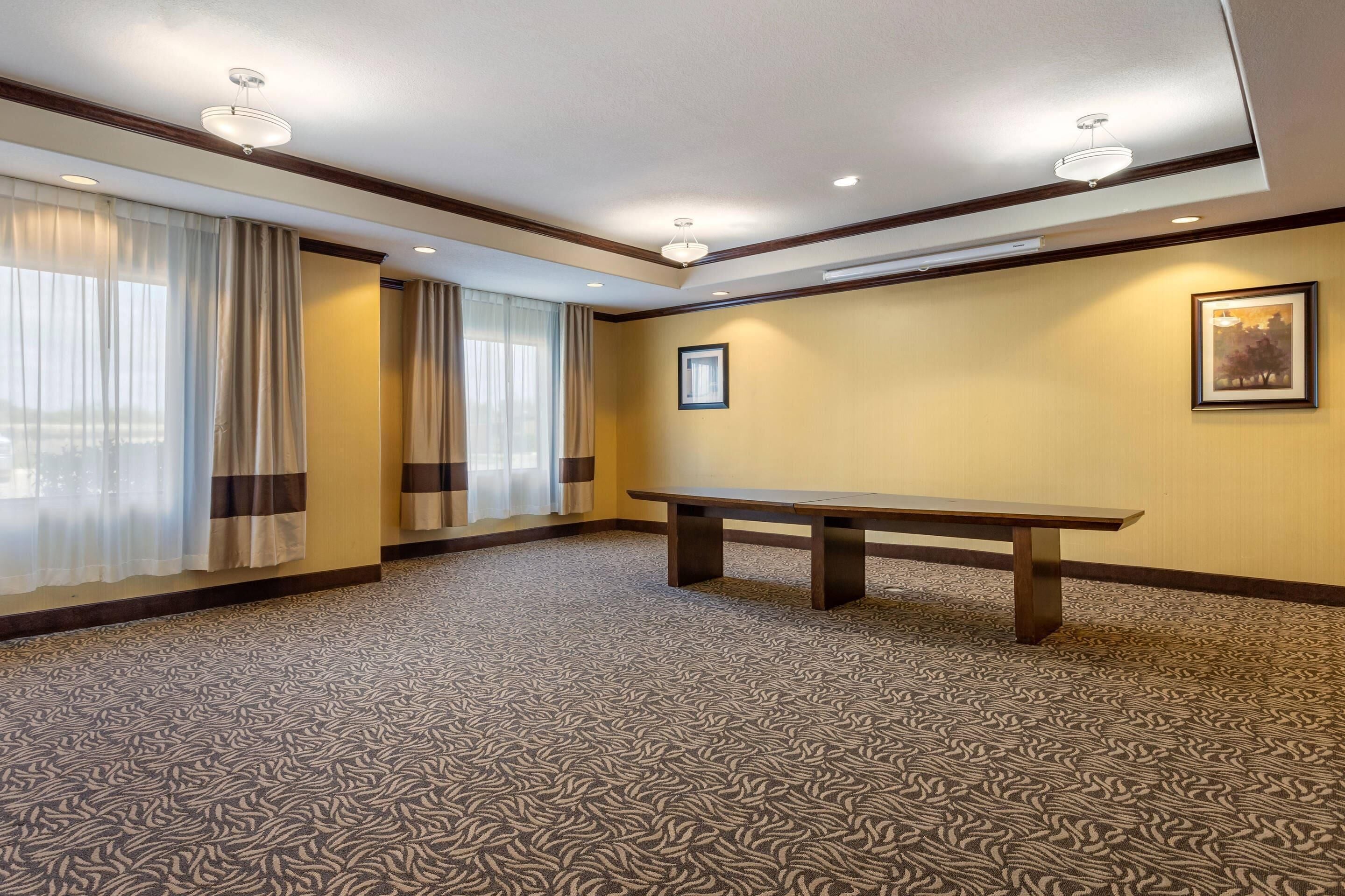A conference room with a patterned carpet, a wooden table, and curtains on the windows.