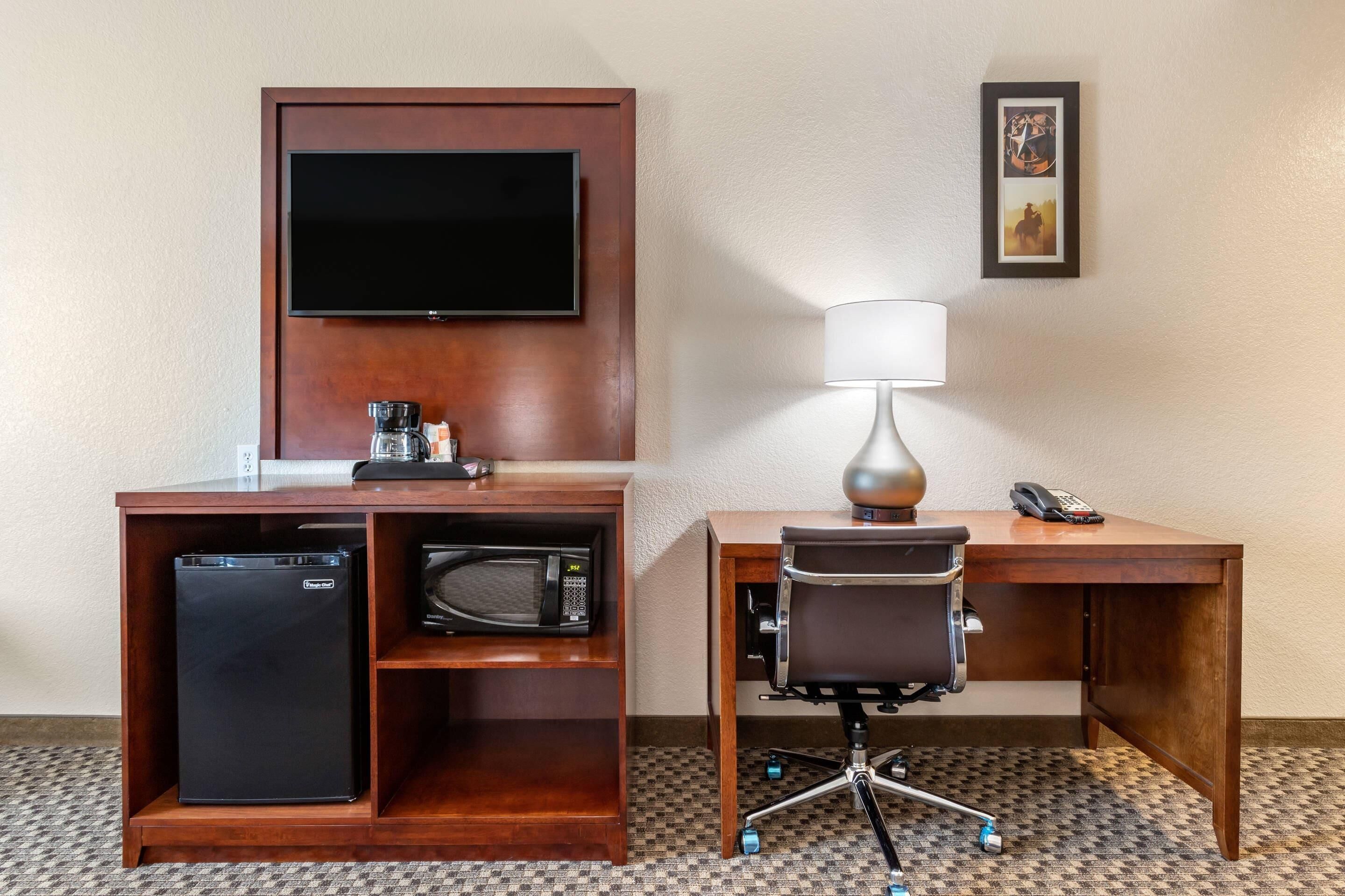 Habitación de hotel con escritorio, silla, televisor, cafetera, microondas y teléfono.