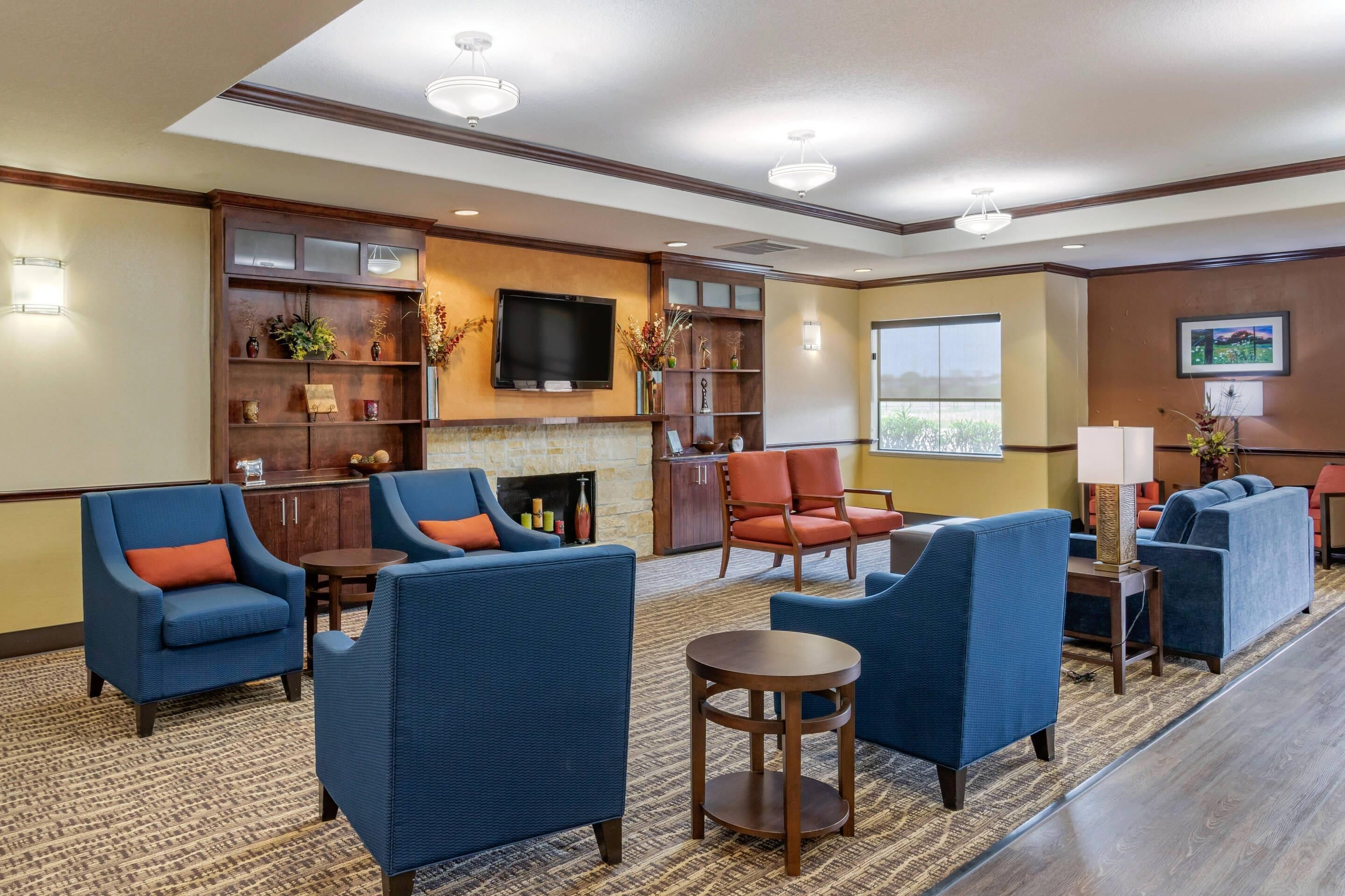 A hotel lobby with blue armchairs, a fireplace, a flat-screen TV, and a large window.