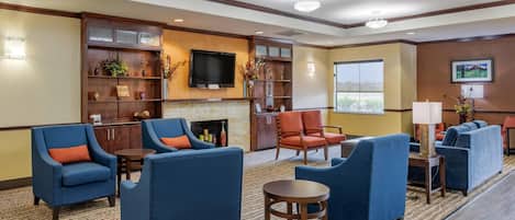 A hotel lobby with blue armchairs, a fireplace, a flat-screen TV, and a large window.
