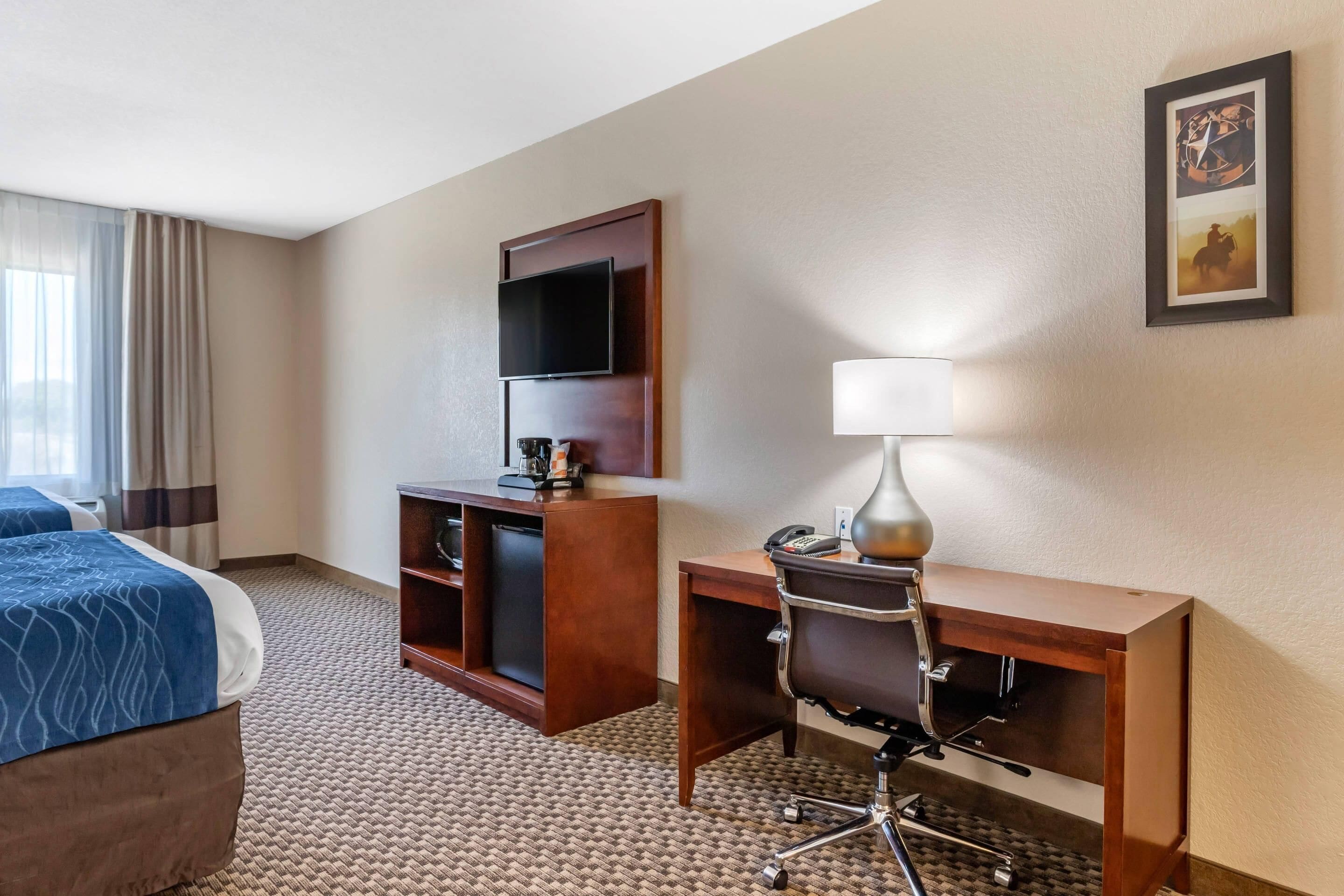 A hotel room with a bed, a desk with a chair, a television, and a lamp.