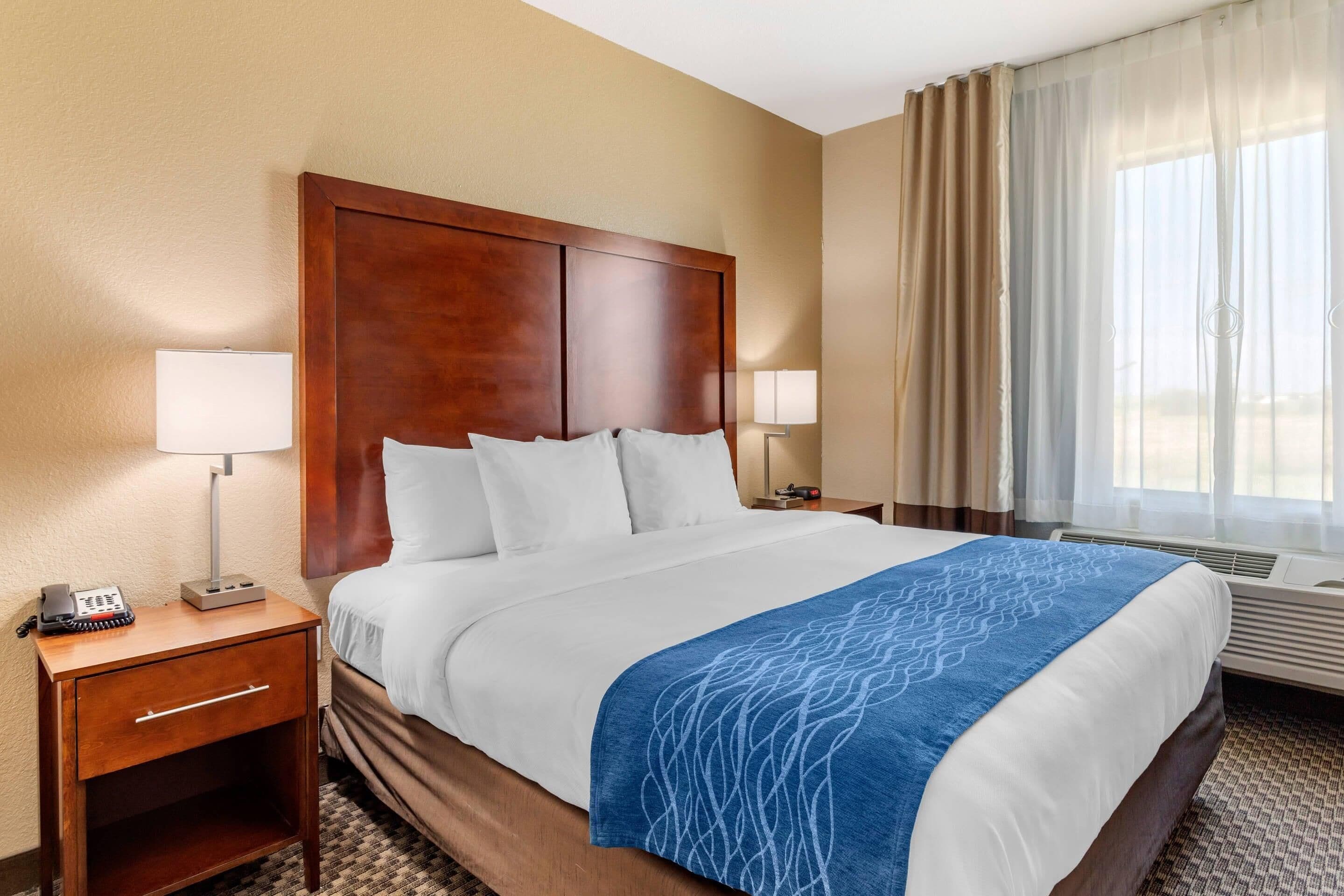 A hotel room with a large bed, two bedside tables, a desk, and a window with curtains.