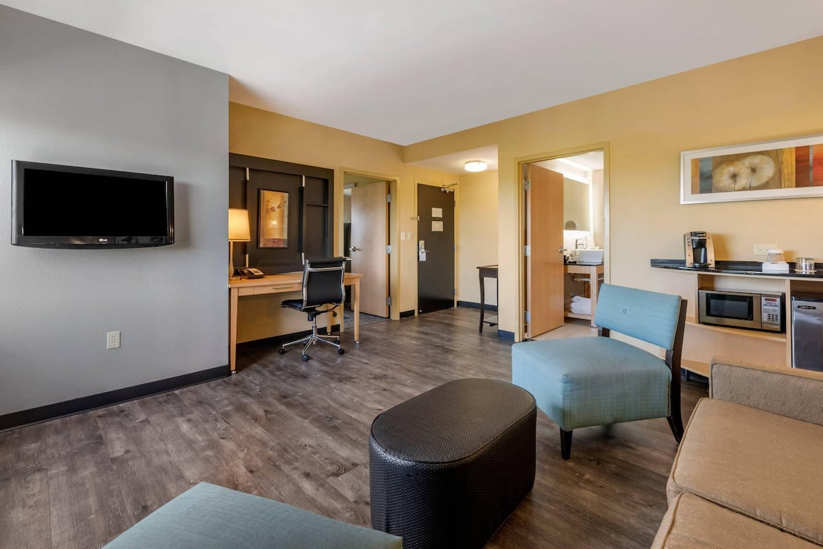 Habitación de hotel con televisor de pantalla plana, escritorio, silla, sofá, reposapiés y kitchenette.